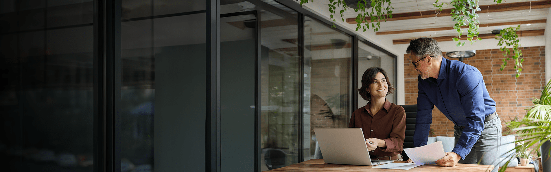 A professional man and woman talking through documents on a modern office balcony.