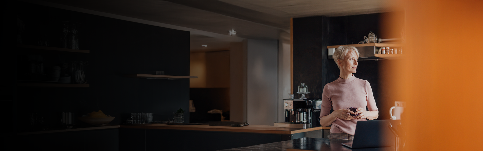 An older lady stood in her modern kitchen looking out of the window.