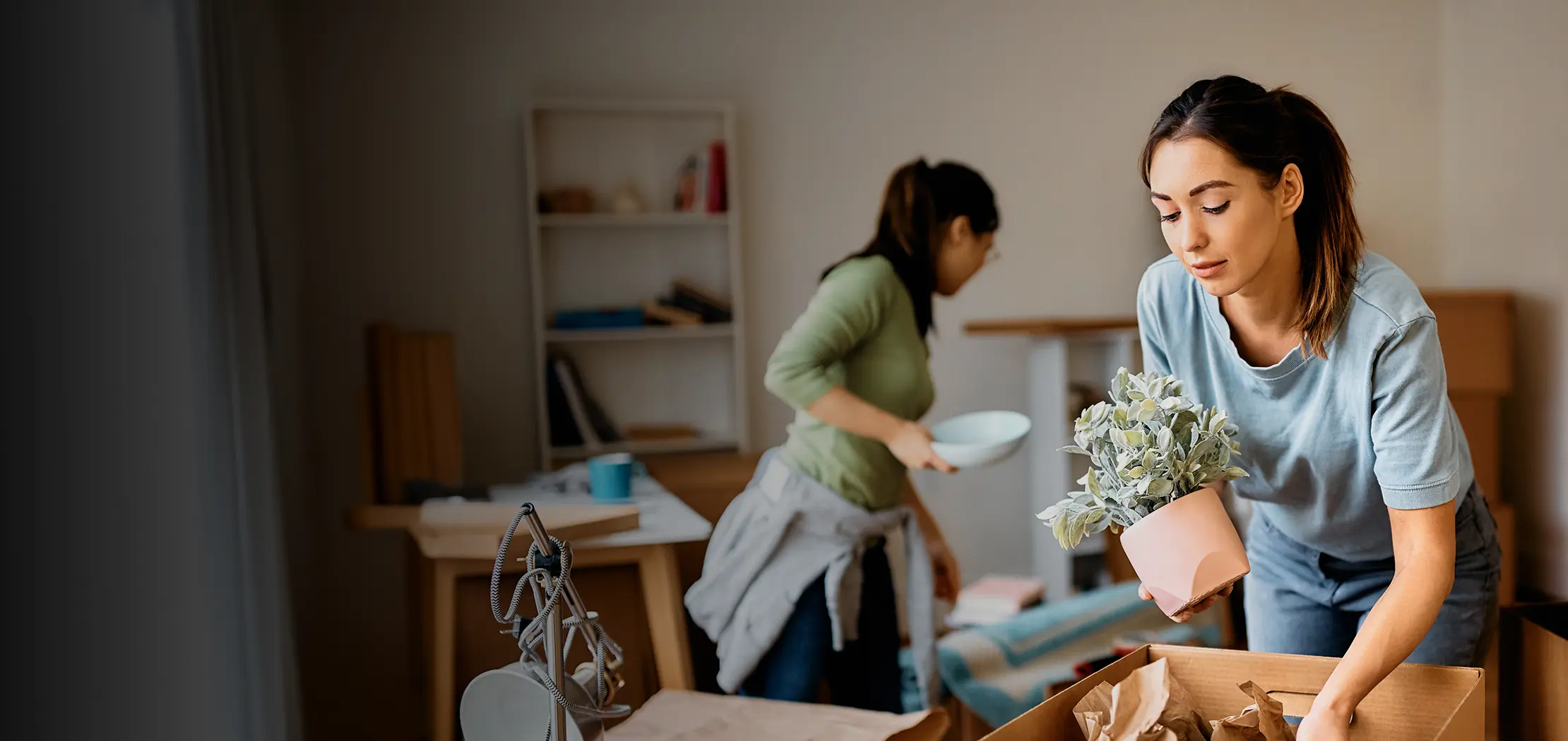 Two women packing items up in boxes.