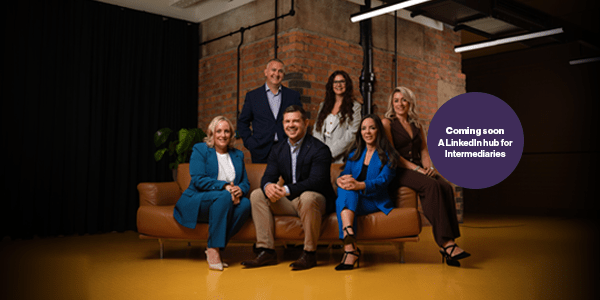 A wide shot of the senior leadership team sitting on a leather couch in front of a red brick wall with a purple circle over the top of it saying coming soon a LinkedIn hub for intermediaries.