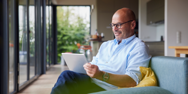 An older man smiling whilst sat on a sofa looking at his iPad.