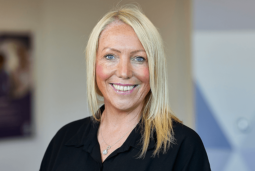 A woman with mid-length blonde hair smiling wearing a black blouse.