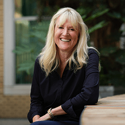 Andrew Dalton with long blonde hair smiling sat on a chair.