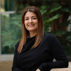Cheryl Brough with long brown hair smiling leaning on table.