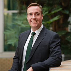 Chris Adams wearing a suit sat smiling.