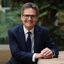 Dave Sutherland smiling wearing a navy blue suit and tie with a white shirt.