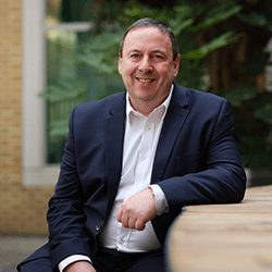 Gary Beckett smiling wearing a blue suit sat down.