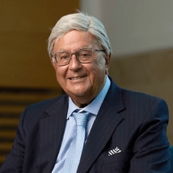 A professional male with short grey hair and glasses smiling wearing a blue blazer and light blue shirt.