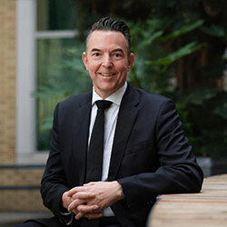 Richard Rowntree with short black hair smiling wearing a suit.