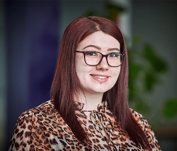 A woman with medium length red hair smiling wearing glasses and a cheetah print blouse.