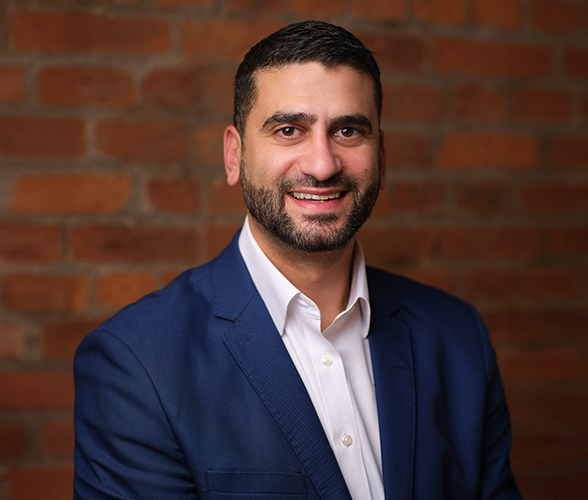 Andy Neo with short brown hair and a beard smiling in front of a red brick wall.
