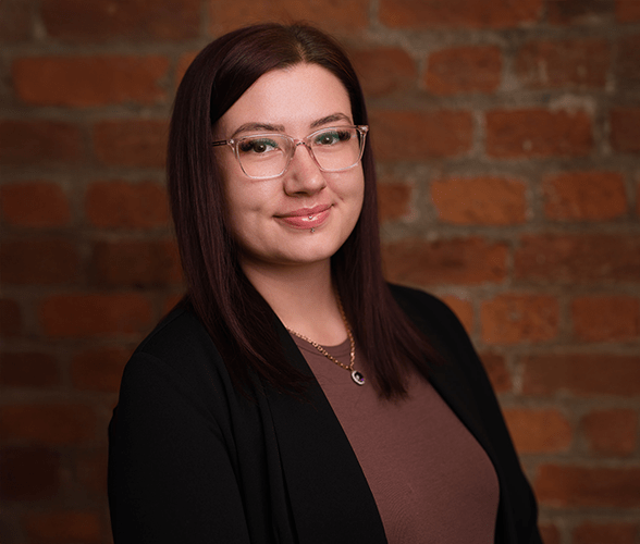 Charlotte Wilson with medium length dark red hair smiling in front of a red brick wall.