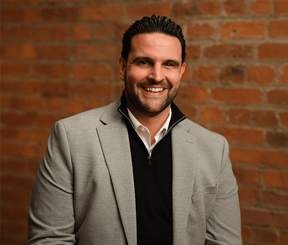 Dan Narwal with short black hair smiling in front of a red brick wall.