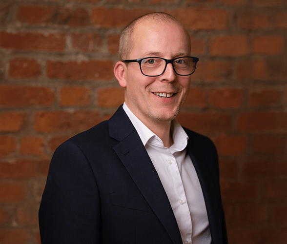 Gareth Wilde smiling in front of a red brick wall.