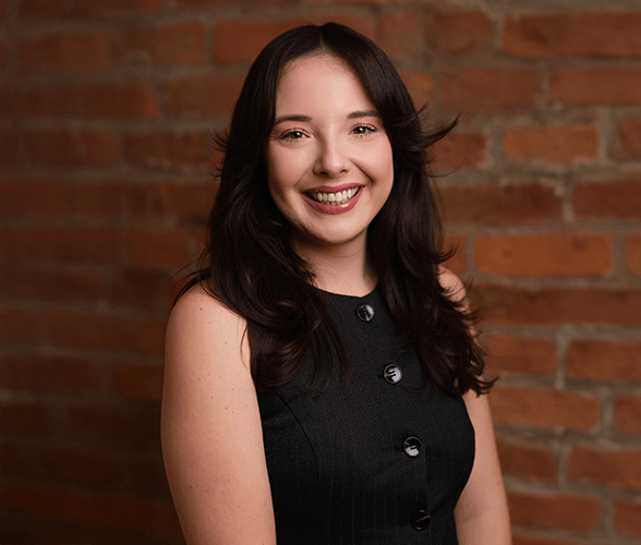 Kerry Jordan with long brown hair smiling in front of a red brick wall.