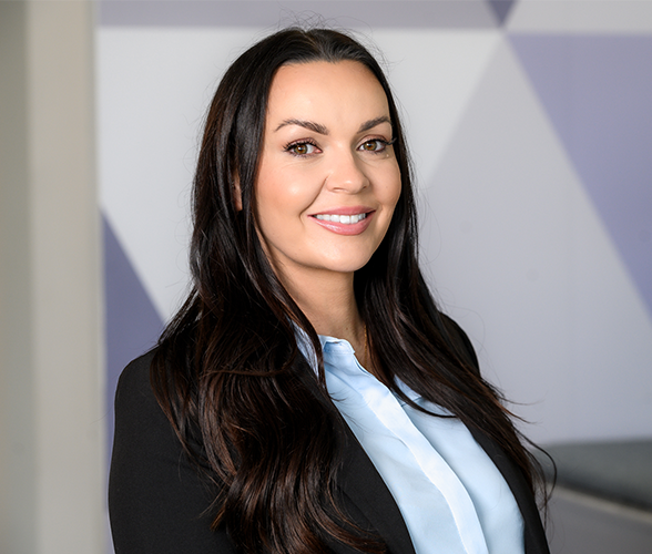 A woman with long brown hair smiling wearing a black blazer and a blue shirt.
