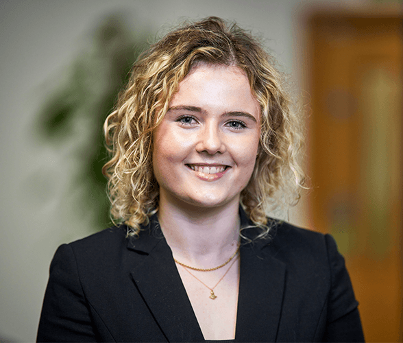 A young woman with short curly hair smiling wearing a black blazer.