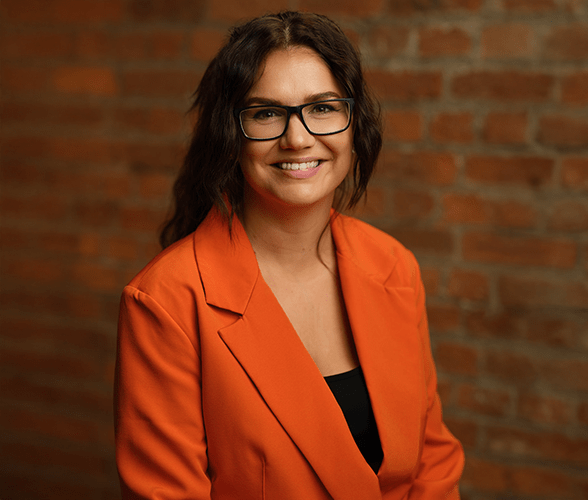 Michelle Walsh with long brown hair smiling in front of a red brick wall.