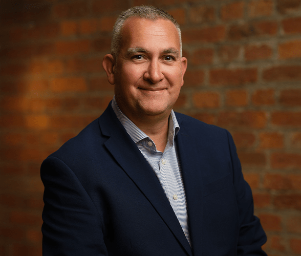 Nick Parker with short grey hair smiling in front of a red brick wall.