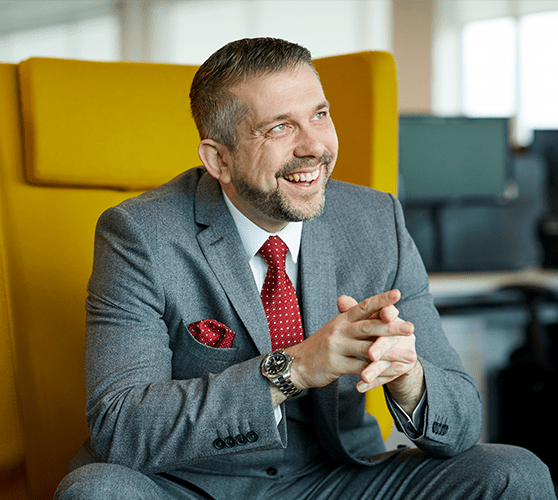 A man with grey hair and a beard smiling wearing a grey suit.