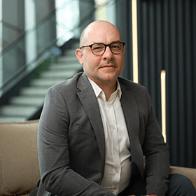 A mid-shot of Graham Noctor wearing glasses and smiling wearing a smart suit.