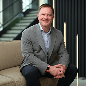 A mid-shot of Scott Clay with short brown hair smiling wearing a smart suit.