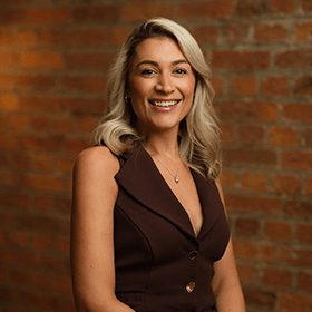 Abi Pickford with long blonde hair smiling in front of a red brick wall.