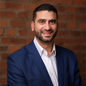 Andy Neo with short brown hair and a beard smiling in front of a red brick wall.