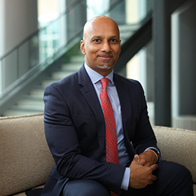 A mid-shot of Arun Jeyarajah smiling wearing a smart suit.