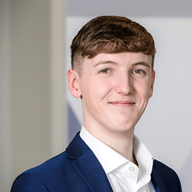 A young man smiling with short brown hair wearing a navy blue blazer and white shirt.