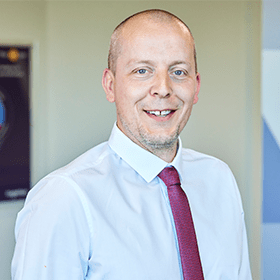 A bald man smiling wearing a white shirt and red tie.