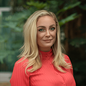 A mid-shot of Kayleigh Simpson with blonde hair and a bright coral blouse smiling.