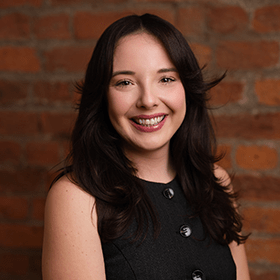 Kerry Jordan with long brown hair smiling in front of a red brick wall.