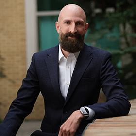 A bald man with a brown beard smiling wearing a suit.
