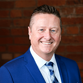 Martin Bloe with short grey hair smiling in front of a red brick wall.
