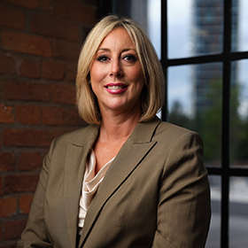A woman with a short blonde bob smiling wearing a green suit smiling.
