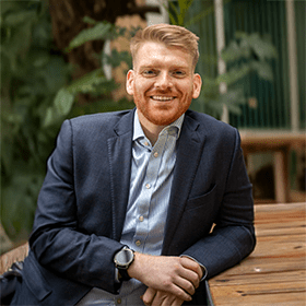 A mid-shot of Michael Slattery with ginger hair smiling with a suit on.