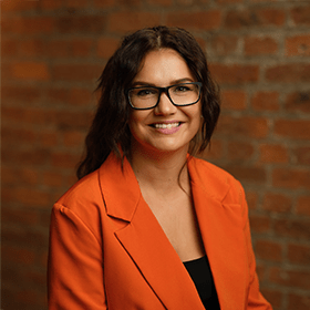 Michelle Walsh with long brown hair smiling in front of a red brick wall.