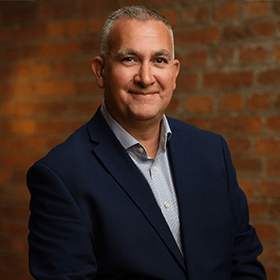 Nick Parker with short grey hair smiling in front of a red brick wall.