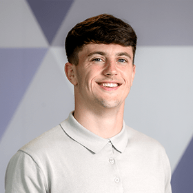 A young man with short dark brown hair smiling wearing a light grey shirt.