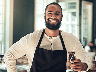 A barber smiling whilst holding some clippers.