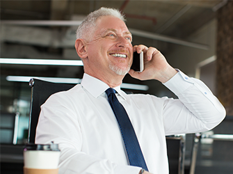 An older man with grey hair smiling whilst on the phone.