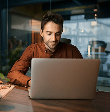 A businessman sat in a modern office at a desk whilst on a laptop.