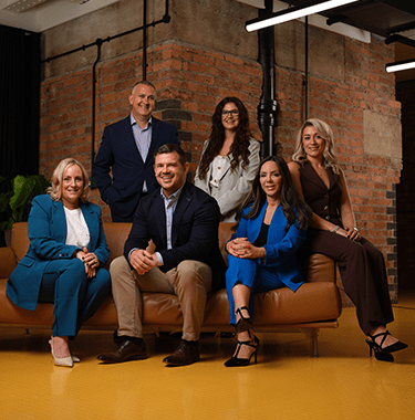 A group of six team leaders sat on a couch in a modern warehouse.