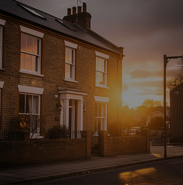 A wide shot of a modern house from the outside on a street whilst the sun is setting in the background.