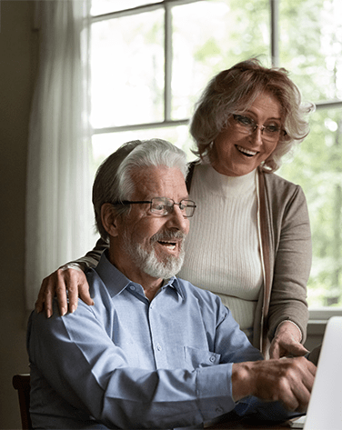 An older couple looking at a laptop together smiling.