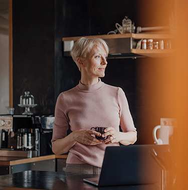 An older lady stood in her modern kitchen looking out of the window.