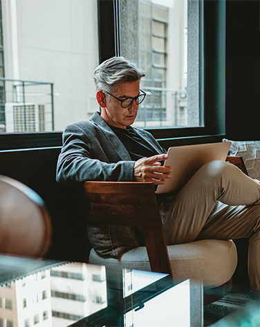 An older man sat in a chair looking at a laptop on his lap.