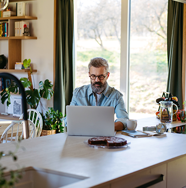 An older man sat in his modern home on a laptop.