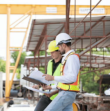 Two builders in high vis jackets looking through documents on a building site.